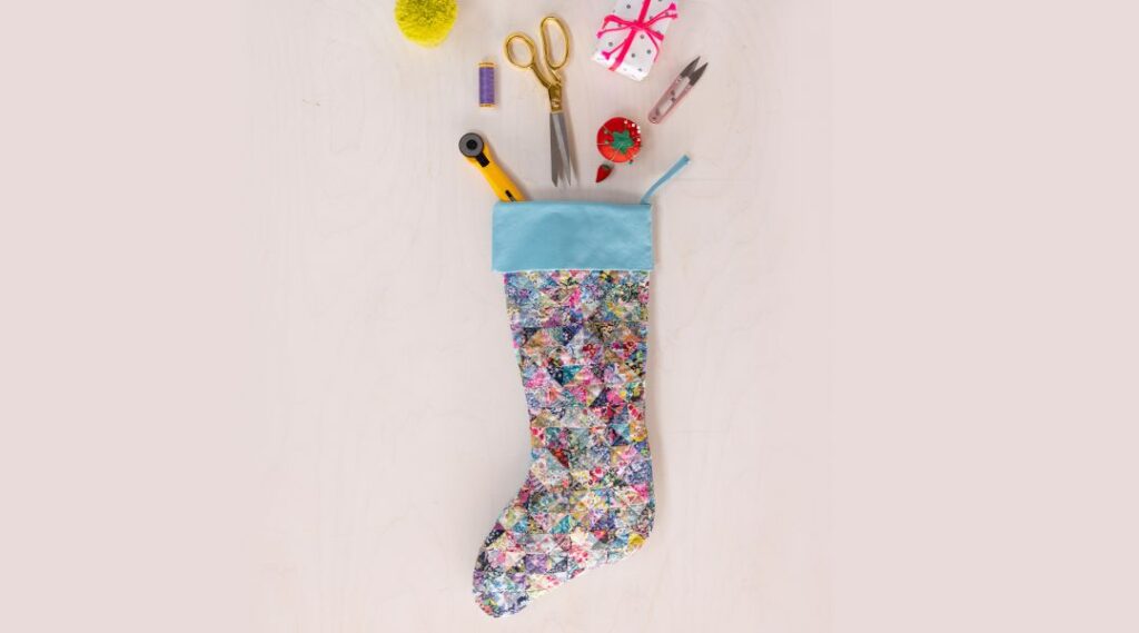 A colorful quilted stocking filled with sewing tools and accessories against a light background.