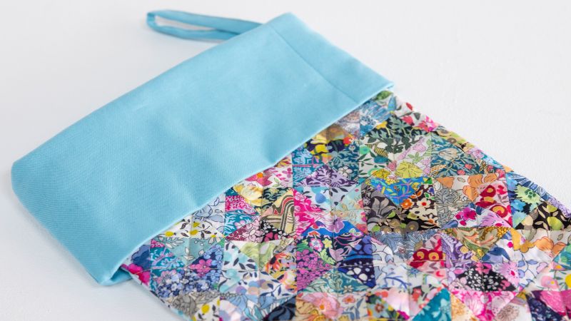 A colorful quilted pouch with a light blue top and handle lies on a white surface.