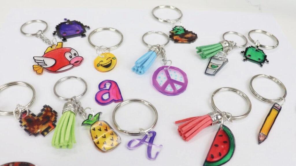 A collection of colorful keychains featuring various designs such as emojis, letters, fruits, and peace signs.