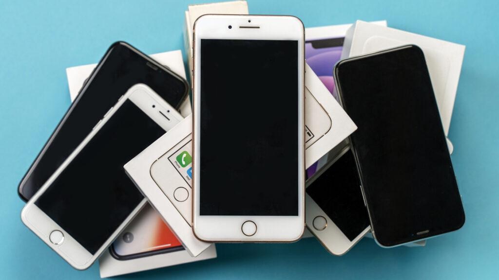 A pile of smartphones and their boxes arranged on a light blue surface.