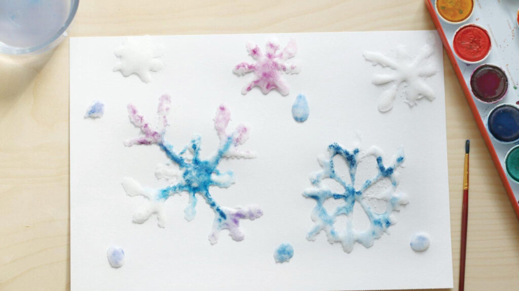 A painting of colorful snowflakes on white paper, made with watercolor and salt.