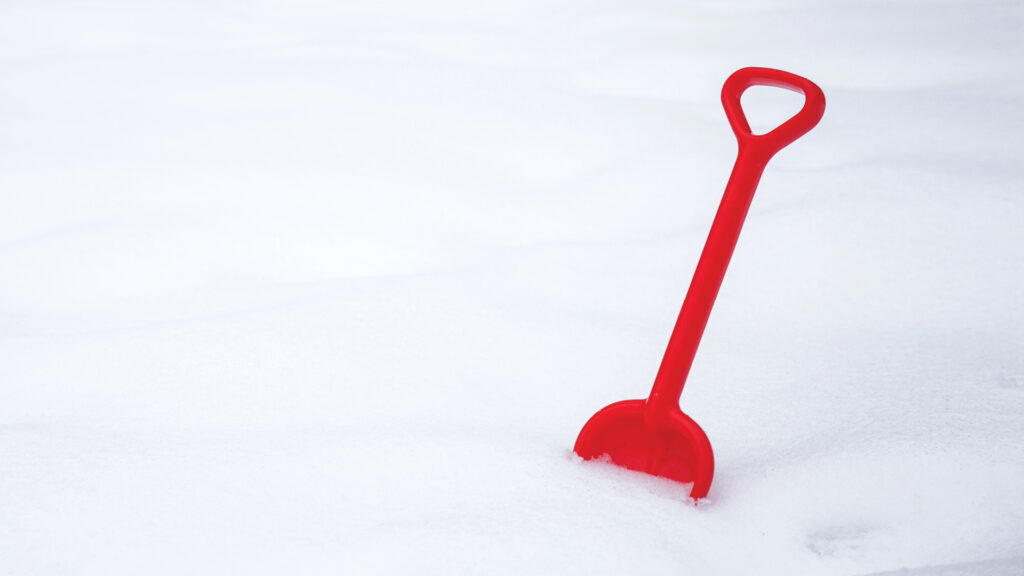 A red plastic shovel stuck upright in a field of smooth, untouched white snow.