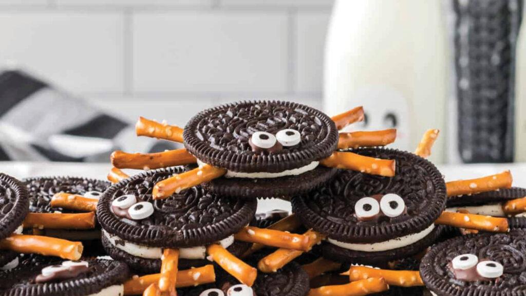 Oreos with pretzel stick legs and candy eyes arranged to look like cute spiders on a table.