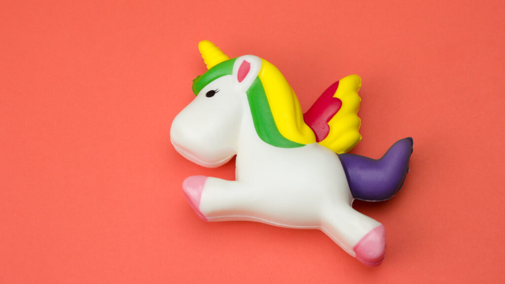 A colorful unicorn toy with wings on a solid coral background.