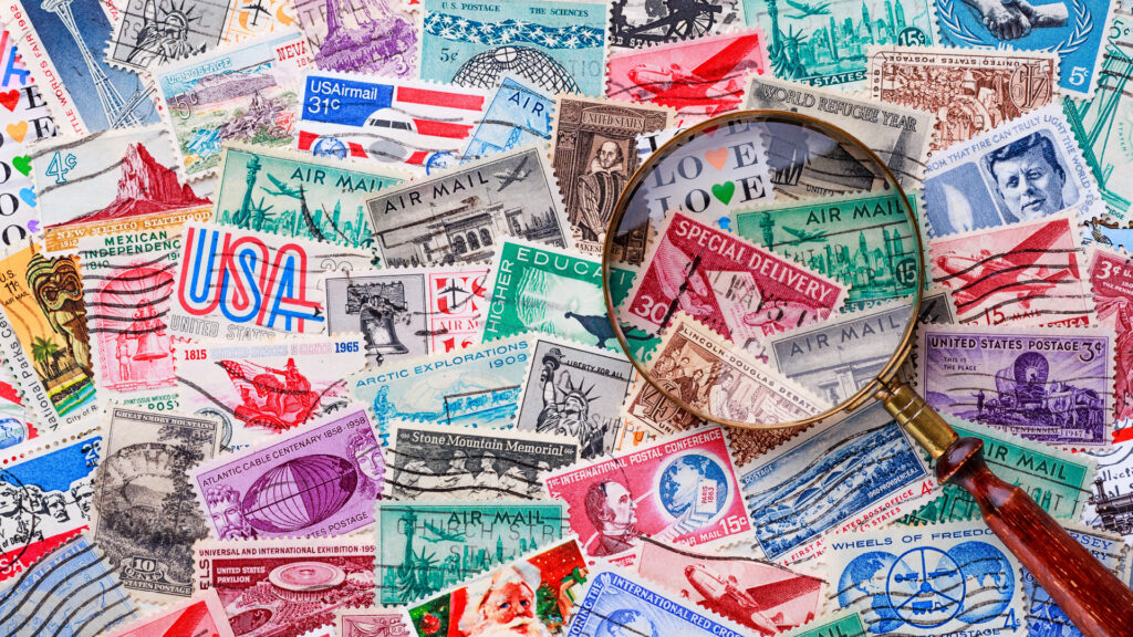 Magnifying glass over colorful vintage postage stamps scattered across a flat surface.