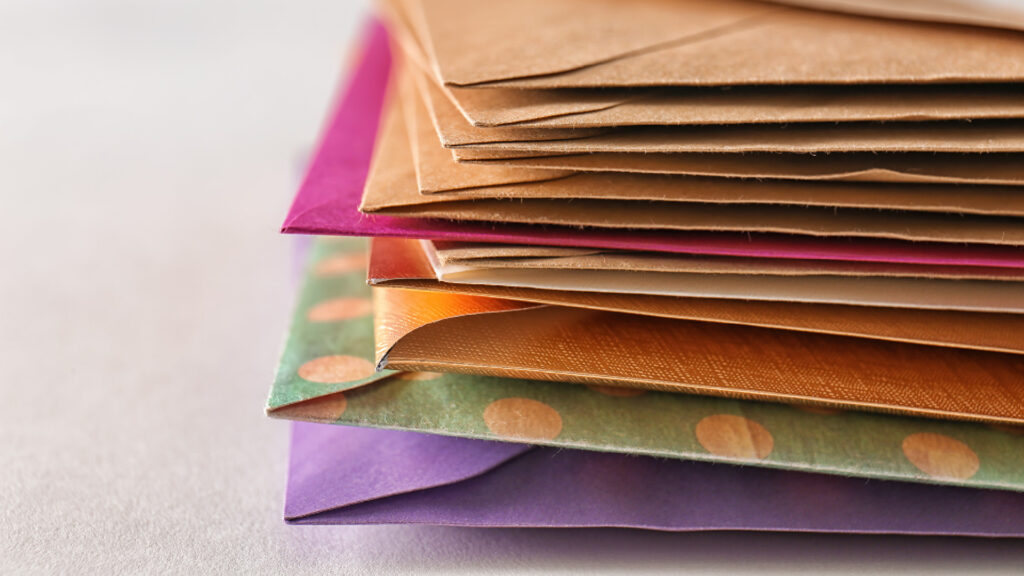 A stack of colorful envelopes in different patterns and colors, including purple, brown, and green with polka dots.