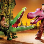 Two actors in animal costumes, one as a crocodile and one as a hippo, perform on a colorful stage.