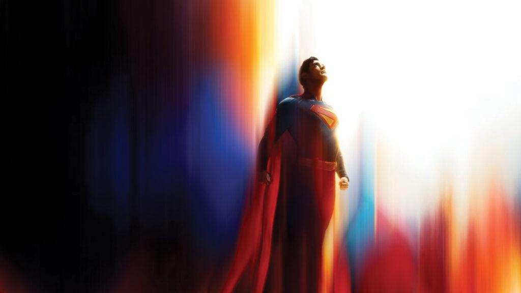 Superman stands heroically with light shining above, his red cape flowing behind against a colorful background.