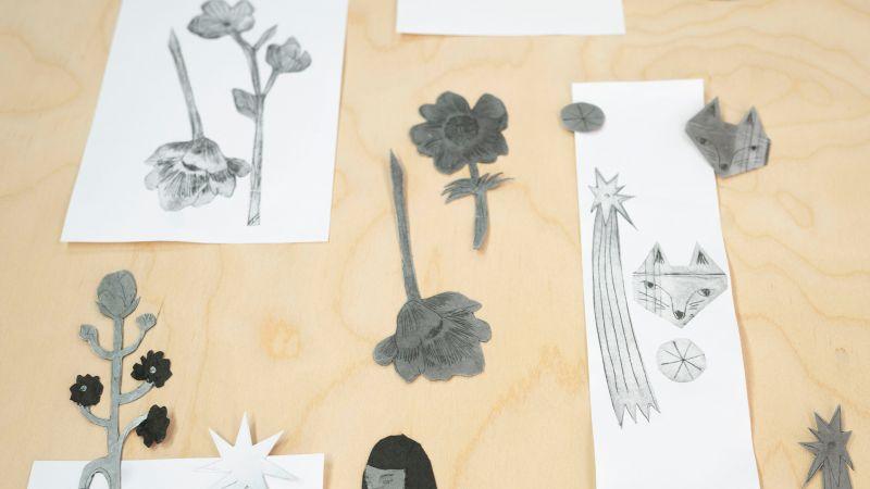 Black and white cut-out flower and star illustrations laid out on a wooden surface.