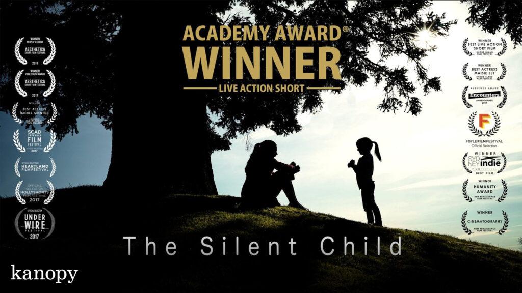 Two people, an adult and a child, sit and stand under a large tree with award logos and "The Silent Child" title.