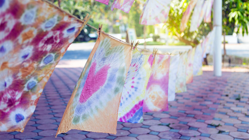 Colorful tie-dye fabrics hang on a line with clothespins outdoors on a sunny day.