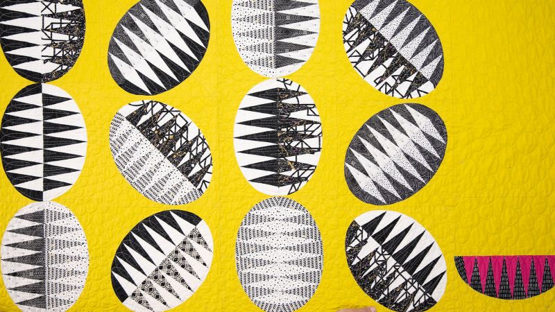 Abstract artwork with black and white patterned ovals on a bright yellow background.