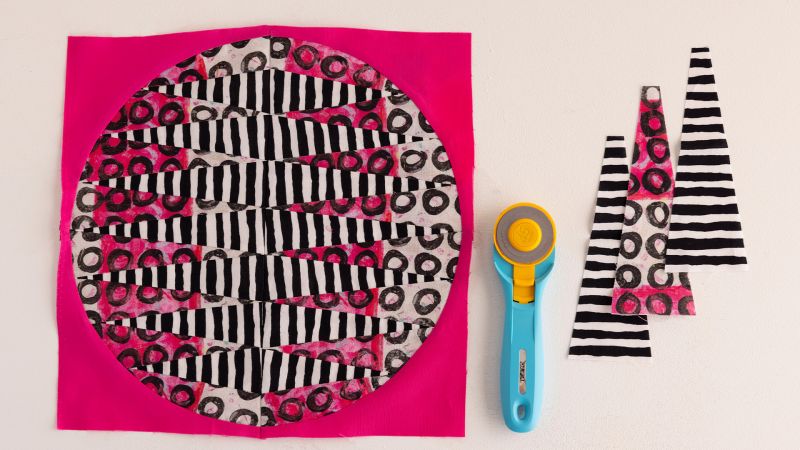 Abstract black, white, and pink fabric pieces and a blue rotary cutter on a white surface.
