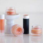 Various lip balm containers on a white surface and pedestal stand.