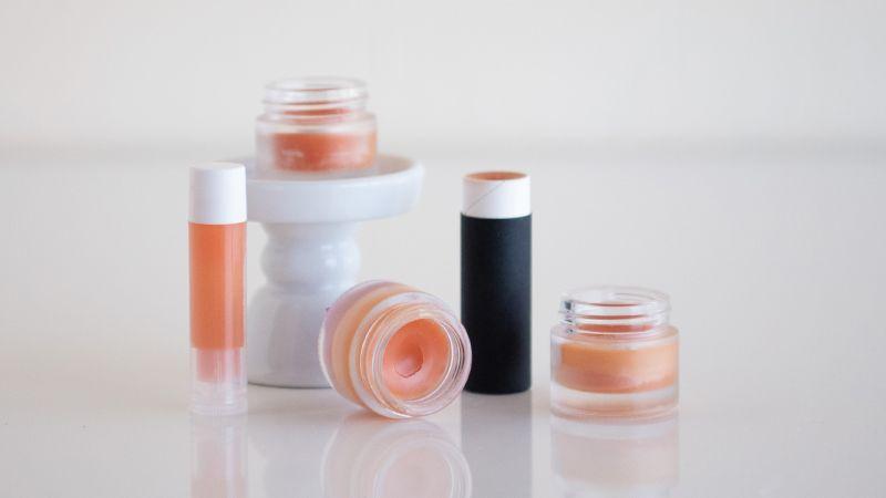 Various lip balm containers on a white surface and pedestal stand.