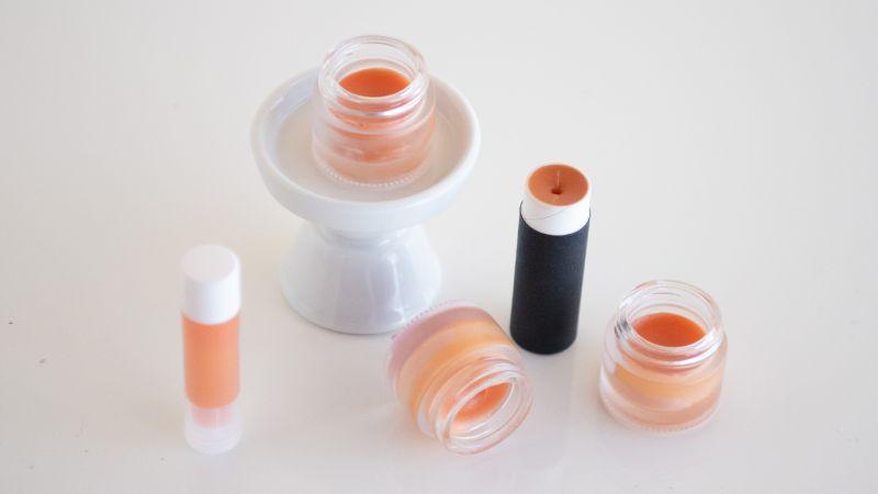 Various lip balms and a lipstick on a white surface, one in a white stand.