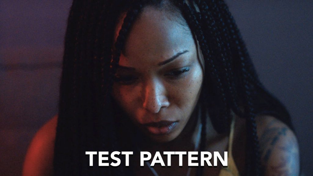 A woman with braided hair looks down with a serious expression; text at the bottom reads "TEST PATTERN.