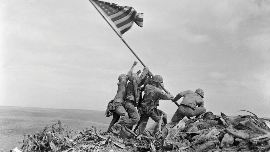 Six soldiers raise the American flag atop a rocky hill during the Battle of Iwo Jima in World War II.