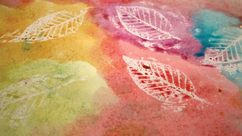 White leaf prints on a colorful watercolor background with shades of pink, yellow, orange, and blue.