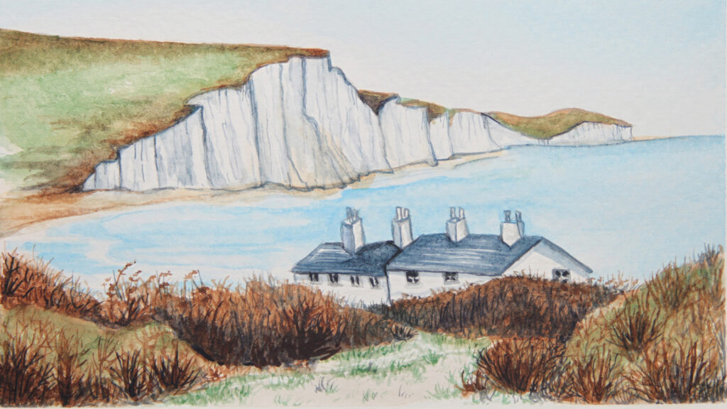 Cottages by the sea with white chalk cliffs and grassy hills in the background, under a clear sky.
