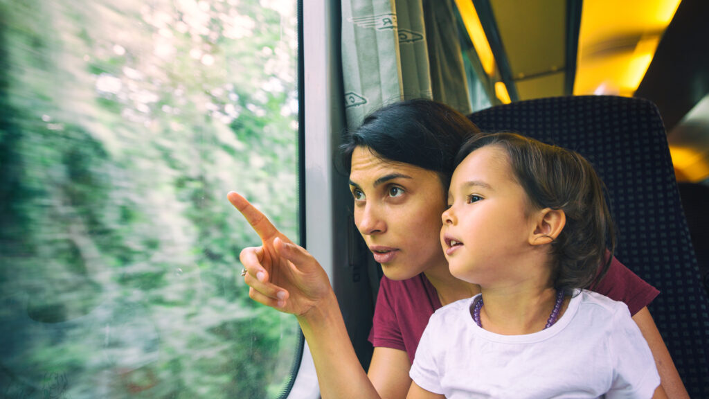 Woman and child sit on a train, looking out the window. The woman points at something outside.