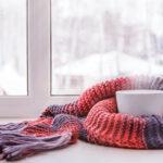 A steaming mug nestled in a cozy red and purple knitted scarf by a snowy window.