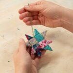 Hands holding a colorful, folded paper star ornament on a wooden table.