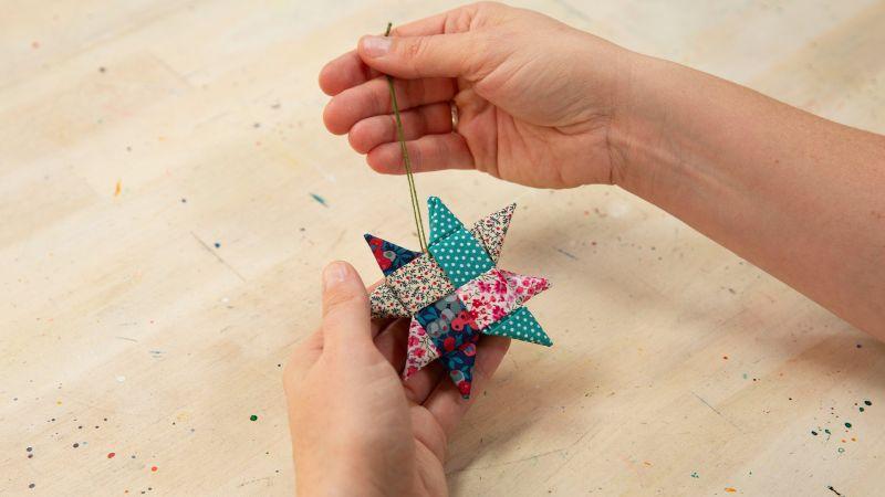 Hands holding a colorful, folded paper star ornament on a wooden table.